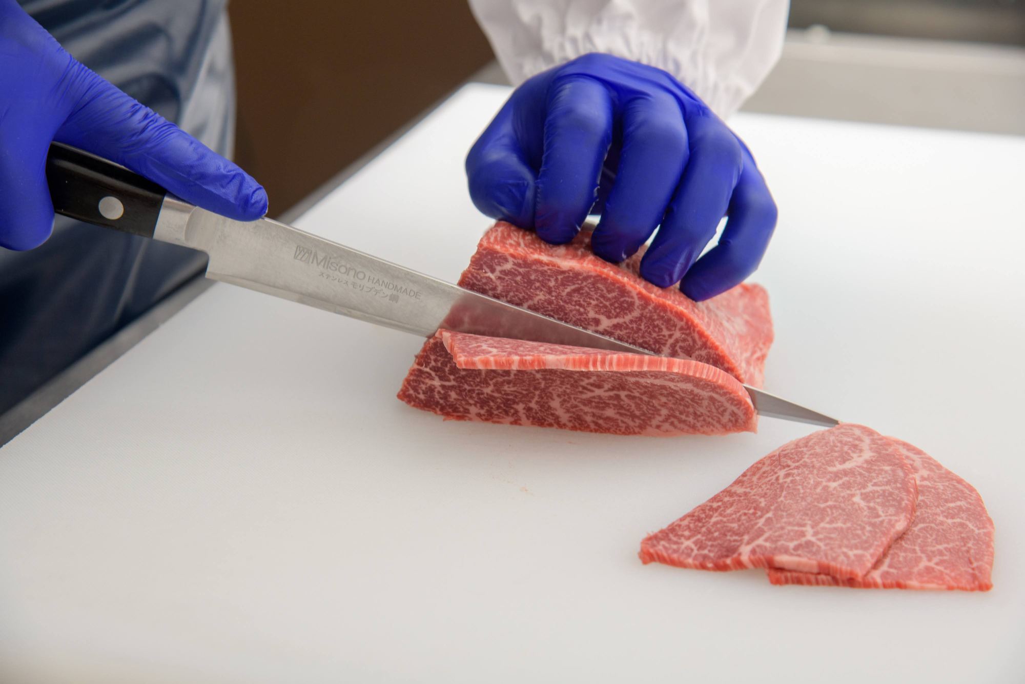 手袋を着けた作業者が肉を切り分ける手元